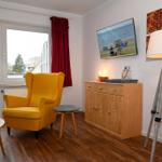 Ein Raum mit gelbem Sessel, Holzboden und TV an der Wand.