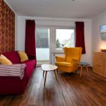 Ein Wohnzimmer mit rotem Sofa, gelber Sessel und Holzboden. An der Wand hängt ein Fernseher.