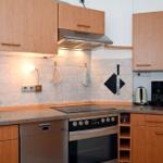 Küche mit Holzschränken, Spüle, Kochfeld und Backofen. Auf Arbeitsfläche stehen Kaffeemaschine und Wasserkocher.