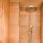 Dusche mit Regenduschkopf und Handbrause in Steinwandverkleidung.