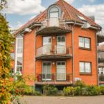 Rotes Backsteingebäude mit Balkonen und Dachfenstern, umgeben von Grünflächen.