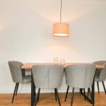 Esstisch mit vier Stühlen, Pendelleuchte und Stehlampe vor strukturiertem Wandbezug.