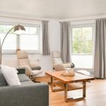 Wohnzimmer mit Sofa, zwei Sesseln, Tisch und Fenstern zum Balkon.