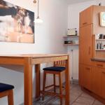 Küche mit Holztisch, Stühlen und Küchenschränken. Wandbild zeigt Kaffeemaschine.