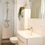 Badezimmer mit Dusche, Waschbecken und Toilette. Weiße Fliesen und moderne Einrichtung.