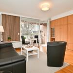 Wohnzimmer mit Sofa, Sessel, Tisch und Holzmöbeln. Durchgang zur Terrasse.