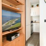 TV in Holzregal, Küche mit weißen Schränken und Kacheln