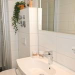 Badezimmer mit Dusche, Waschbecken und Spiegel. Weiße Fliesen und moderne Armaturen.