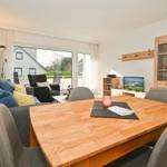 Essbereich mit Holztisch und Stühlen. Wohnbereich mit Sofa, Fernseher und Glasvitrine.