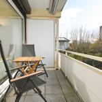 Terrasse mit Tisch und zwei Stühlen, Blick auf Bäume und Gebäude.