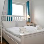 Schlafzimmer mit weißem Bett, zwei Nachttischen und blauen Vorhängen an einem Fenster.