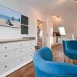 Wohnbereich mit blauen Sesseln, Küchenbereich und Fernseher an der Wand.