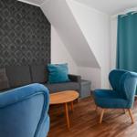 Wohnzimmer mit Sofa, zwei blauen Sesseln und Holztisch unter Dachschräge.