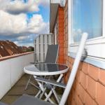 Terrasse mit Tisch und Stühlen, Blick auf Dächer und Himmel.