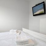 Das Schlafzimmer mit weißem Bett und TV an der Wand.