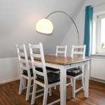 Esstisch mit vier Stühlen, Bogenlampe und Fenster mit blauen Vorhängen.