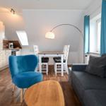 Wohnung mit Essbereich, Sofa, blauer Sessel und Küchenbereich unter Dachschräge.