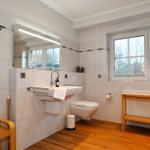 Badezimmer mit Waschbecken, Toilette und Fenster. Holzfußboden und Holzregal.