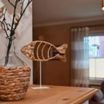 Auf dem Tisch steht eine geflochtene Vase mit Zweigen und eine Fischdekoration.