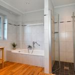 Bad mit Badewanne, Dusche und Holzboden. Fenster mit Pflanze.