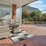 Terrasse mit Sitzgruppe, Tisch und Teppich auf Steinplatten. Hintergrund mit Garten und Steinmauer.