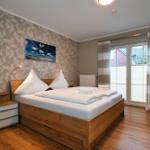 Schlafzimmer mit Holzbett, Wandbild und Schiebetür zum Balkon.