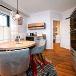 Essbereich mit runder Tisch, Stühlen und Küchenzeile. Holzfußboden und Fenster mit Jalousien.