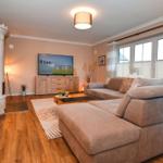 Wohnzimmer mit Sofa, Fernseher und Kaminofen. Holzboden und große Fenster.