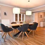 Esszimmer mit Holztisch, dunklen Stühlen und zwei Hängelampen. Durchgang zur Schlafzimmerseite.