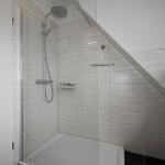 Dusche mit Glaswand, Duschbrause und Holzregal an der Wand