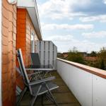 Terrasse mit Stuhl und Tisch, Blick auf Dächer und Bäume unter blauem Himmel.