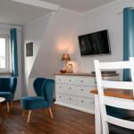 Zimmer mit zwei blauen Sesseln, Schreibtisch, TV und Holzboden.