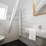 Badezimmer mit Toilette, Waschbecken und Dachfenster. Weiße Fliesen und Holzspiegel.