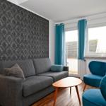 Wohnzimmer mit grauem Sofa, blauen Sesseln und Holztisch. Fenster mit blauen Vorhängen.