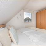 Schlafzimmer mit Dachschräge, Bett, Kleiderschrank und Fenster mit Blick auf Dach.