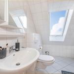 Badezimmer mit Waschmaschine, Toilette und Dachfenster. Weiße Fliesen und Spiegel.