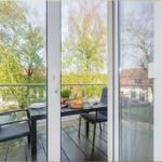 Terrasse mit Tisch, Stühlen und Frühstücksgeschirr. Blick auf Bäume und Gebäude.