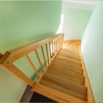 Holzgetreppe mit Geländer führt nach oben. Wände sind hellgrün gestrichen.