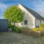 Ein Haus mit Garten, Holzzaun und Steinpflaster. Links steht ein Metallschuppen.