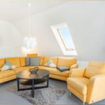 Ein Wohnzimmer mit gelbem Sofa, runden Tisch und Dachfenster.