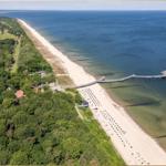 Aussicht auf Strand, See und Pier mit grüner Umgebung.