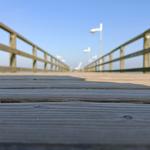 Holzbrücke mit Geländer und Straßenlaternen unter blauem Himmel
