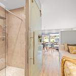 Dusche mit Glaswand, Schlafzimmer mit Bett und TV, Essbereich mit Tisch und Stühlen.