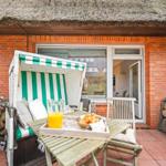 Terrasse mit Strandkorb, Tisch und Frühstück. Roter Backsteinbau mit Dach aus Stroh.