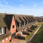 Rote Backsteinhausreihe mit strohgedeckten Dächern und Gartenbereichen.