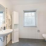 Badezimmer mit Waschbecken, Spiegel, Toilette und Fenster.