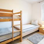 Zimmer mit Doppelstockbett, Schreibtisch und Fenster mit Jalousie.