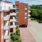 Ferienhaus am Waldbad mit Balkonen und Parkplatz. Grünanlagen und Wald im Hintergrund.