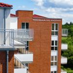 Ferienhaus am Waldbad mit Balkonen und rotem Dach unter blauem Himmel.
