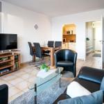 Wohnzimmer mit Sofa, Sessel, Esstisch und TV. Küche im Hintergrund sichtbar.